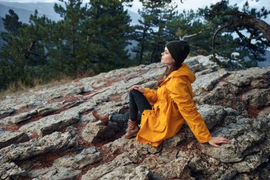 Sarı ceketli bir kadın huzur dolu bir yolculukta dağın tepesinden nefes kesici manzaranın tadını çıkarıyor.