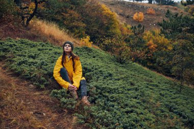 Güneşli bir sonbahar gününde, renkli yapraklarla çevrili tepelerde huzurlu bir anın tadını çıkaran bir kadın.