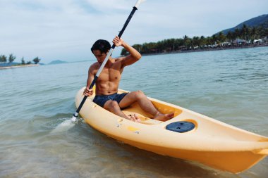 Kano Macerası: Mutlu bir Asyalı elinde küreğiyle Tropikal bir plajda Aktif Bir Açık Hava Tatili Yapıyor