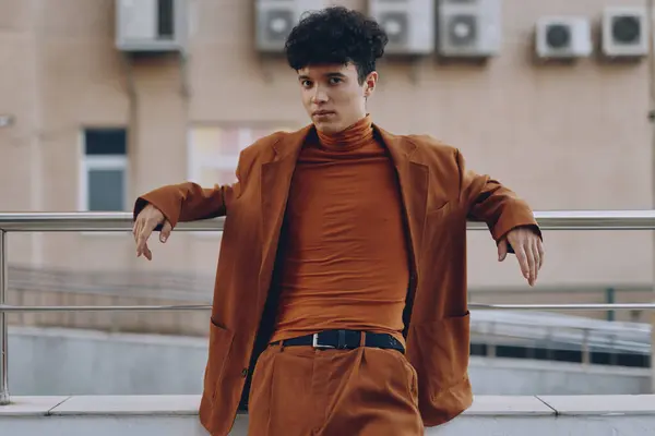 stock image A fashionable young man wearing a brown suit and turtleneck stands against a building backdrop, exuding modern elegance and urban style