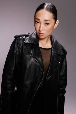 Asian woman black leather jacket posing camera gray background. clipart