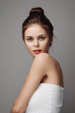 Beyaz elbiseli güzel bir kadın gri arka planda kameraya poz veriyor..