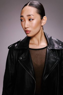 Moda, Asyalı kadın, siyah deri ceket, poz, kamera, gri arka plan. Tarafsız gri bir arkaplan önünde poz veren siyah deri ceketli Asyalı bir kadın..