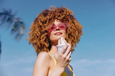 Dondurma tutan neşeli bir kadının parlak görüntüsü, yayılan yaz titreşimleri mavi gökyüzü ve palmiye ağaçları neşe dolu atmosferi yükseltiyor.