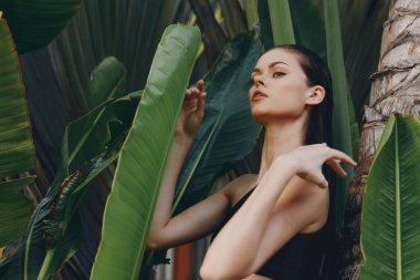 Kendine güvenen bir kadının portresi, bir palmiye ağacının önünde, elleri kalçalarında, tropik bir arka planda poz veriyor.