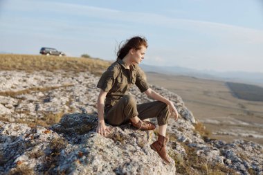 Ayakları havada kayanın üzerinde oturan kadın seyahat sahnesinde arabanın arka planına yaslanıyor.