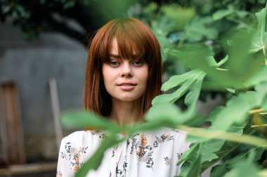 Çevresi yemyeşil, kızıl saçlı sakin bir kadın.