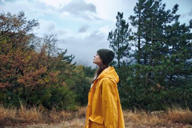 Parlak Sarı Yağmurluklu Kadın Arka planda Ağaçları olan Serene Field 'ın ortasında duruyor