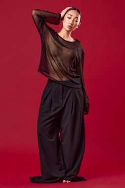 Saf üst ve geniş bacaklı Asyalı kadın elleri kalçasında kırmızı arka planda poz veriyor. Moda konsepti.