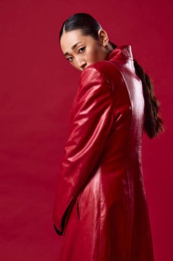 Kırmızı arka planda kırmızı deri ceket giyen Asyalı şık esmer kadın..