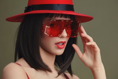 Kırmızı şapkalı, kırmızı elbiseli ve çivili kırmızı güneş gözlüklü bir kadın, kendine güveni ve stili olan yüzünün yan görüntüsü, moda ve yaşam tarzı kavramları için ideal.