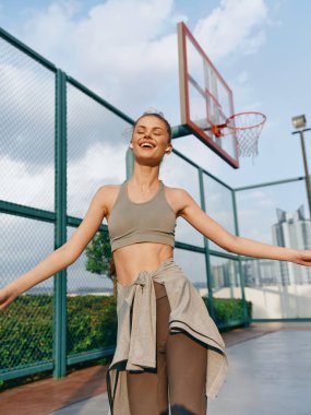 Spor giyim sektöründe enerjik genç bir kadın basketbol sahasında güneşlenirken neşeli bir ifadeyle güneşleniyor.
