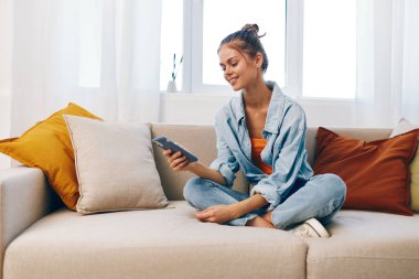 Gülümseyen Kadın Cep Telefonu, Çevrimiçi Oyunlardan Hoşlanıyor ve Oturma Odasında Sohbet Ediyor