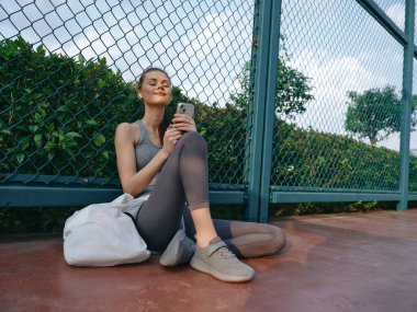 Genç bir kadın, yeşil ve çitlerle çevrili telefonunu kontrol ederken bir anlık dinlenmenin keyfini çıkarıyor.