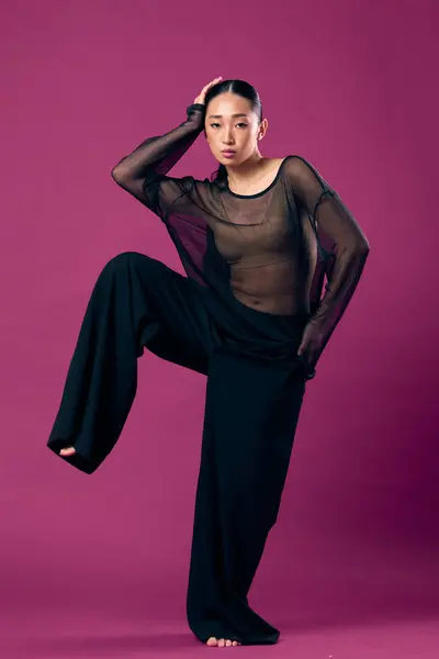 stock image Fashion asian woman in sheer top and wide leg pants posing on purple background with hands on hips and legs spread apart.