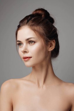 Kalçaları üzerinde elleri ve yüksek topuz saçlı, gri arka planda duran üstsüz genç bir kadın. Güzel ve şık bir kadın portresi..