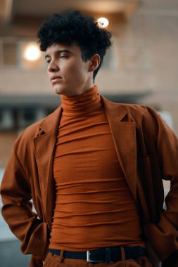 Modaya uygun genç bir adam, kendine güvenen kahverengi balıkçı yaka bir kazak ve uyumlu bir takım elbiseyle modern şehir estetiğini gözler önüne seriyor.