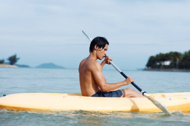 Plajdaki Macera: Genç Asyalı Bir Adam Tropikal Sularda Kano ile Renkli Kano ve Kürek Çekiyor