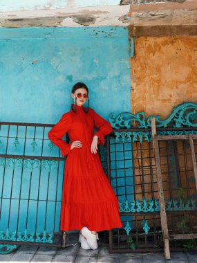 Sofistike bir kadın çarpıcı kırmızı bir elbiseyle özgüven yayar, koyu mavi ve sarı bir arka plana karşı durarak..