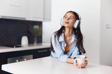 Genç bir kadın, mutfaktaki en sevdiği melodileri huzur içinde dinlerken kulaklıkla müzik dinlemekten zevk alıyor.