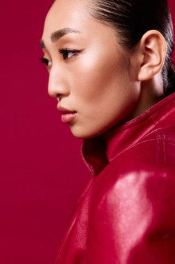 Kırmızı deri ceketli, saçları at kuyruklu, gözleri kapalı, uzaktan bakan Asyalı esmer kadın..