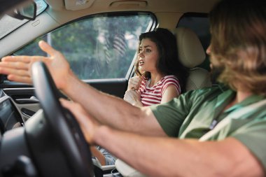 Bir erkek ve kadın hararetli bir şekilde bir araçta tartışıyorlar. İç ayrıntıların arasında güçlü duygular sergiliyorlar.