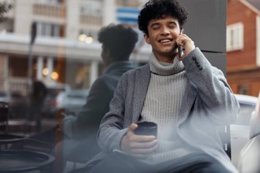 Vitrinin kenarında oturan, elinde kahve fincanıyla konuşan şık bir süveter giyen şık genç adam..