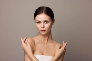 Elleri göğsünde, gri arka planda, boynunda havluyla poz veren genç kadın. güzel ve kendinden emin.