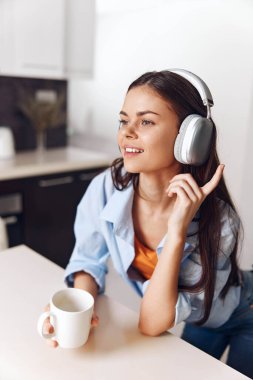 Evde müzik ve kahveden zevk alan genç bir kadın, dinlenirken ve güne başlarken kulaklık dinliyor.