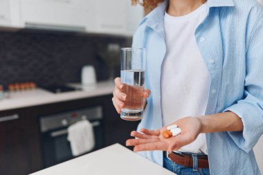 Mutfak tezgahının önünde elinde bir bardak su ve hap tutan kadın.
