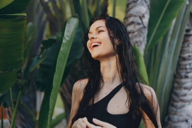 Tropik plaj tatillerinde palmiye ağaçlarının önünde gülümseyen siyah mayolu mutlu kadın.