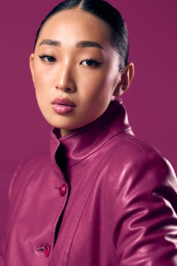 Mor deri ceketli Asyalı esmer, at kuyruklu mor arka planda poz veriyor..