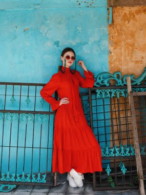 Göz kamaştırıcı kırmızı elbiseli özgüvenli bir kadın canlı mavi bir arka planın önünde zarif bir şekilde duruyor, zarafet ve tarz yayıyor..