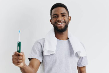 Gülümseyen Afrikalı Amerikalı adam, diş fırçası ve diş macununu el değmemiş beyaz bir zemine karşı tutarak, ağız temizliğini coşkuyla destekliyor..