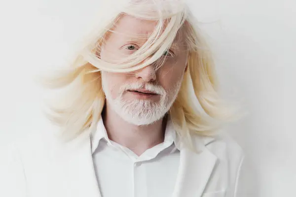 stock image This close up portrait features a man with long white hair and a beard dressed in a white blazer The light, neutral background enhances his striking appearance, creating an elegant and tranquil