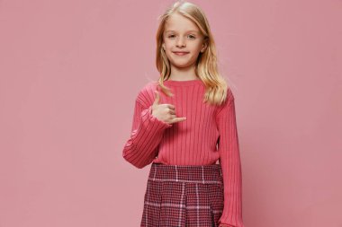 Stüdyoda poz veren zarif pembe elbisesi ve büyük bir gülümsemesi olan genç bir kız. Neşeli ifadesi ve mutlu gözleri çocukluk sevincini canlı bir arka plana yansıtıyor. Güzel ve modaya uygun bir arka plan.