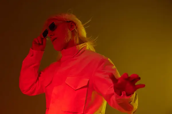 stock image Trendy individual with long white hair and stylish sunglasses striking a pose against a vibrant yellow backdrop The image conveys a sense of confidence, modern fashion, and artistic flair, perfect for