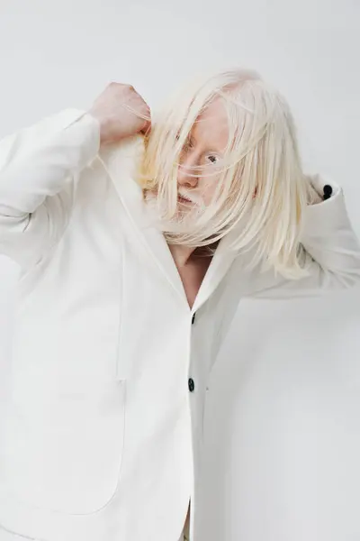 stock image Striking fashion image of a model with long white hair, dressed in a tailored white blazer The minimalist background enhances the focus on the model s distinct look and expressive pose, radiating