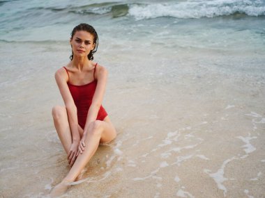 Kırmızı mayo giymiş bir kadın güzel bir güneş yanığıyla kumda oturur ve Bali Adası Sahili 'ndeki tropiklerde okyanusu seyreder. Yüksek kalite fotoğraf