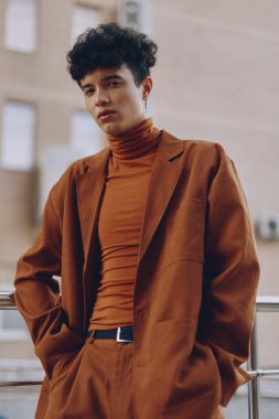 Kahverengi takım elbise ve balıkçı yaka giyen şık genç bir adam şehir zeminine karşı güven yayıyor.