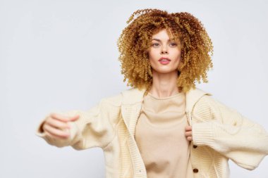 Şık bir model, yumuşak krem rengi hırka giyerken doğal kıvırcık saçlarını sergiliyor. Açık arka plan, moda ve yaşam tarzı tasviri için ideal, hareketli görünümünü geliştiriyor.