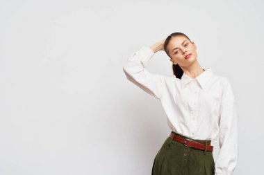 Kendine güvenen bir manken zarif bir şekilde poz verir, beyaz bir gömlek ve yeşil bir etek giyer. Minimalist açık gri arka plan onun şık tarzını ve modern çekiciliğini vurgular.