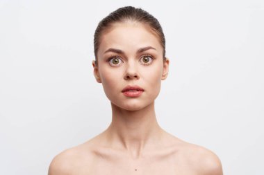 Tarafsız bir ifadeyle şaşırmış genç bir kadının çarpıcı portresi, basit beyaz bir arkaplan karşısında çekilmiş etkileyici gözleri ve doğal makyajı şokun ve entrikanın duygularını vurguluyor.