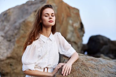 Beyaz elbiseli, dingin genç bir kadın okyanus kıyısında, gözleri kapalı meditasyon yapıyor.