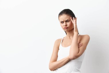 Endişeli genç bir kadın, basit beyaz bir bluz giymiş, somurtkan bir ifade ve kafasında bir el ile, parlak beyaz bir arka plan üzerine kurulmuş, karmaşa duygularını veya endişelerini etkili bir şekilde gösteren