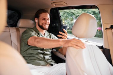 Genç bir adam tesadüfen giyinmiş, arabasının arka koltuğunda görüntülü konuşmanın keyfini çıkarıyor.