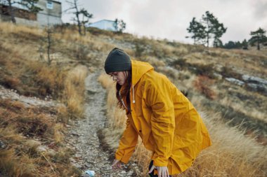 Sarı yağmurluklu bir kadın kırsal bir macerada bir yamaçtan top toplayarak huzurlu bir anın tadını çıkarıyor.