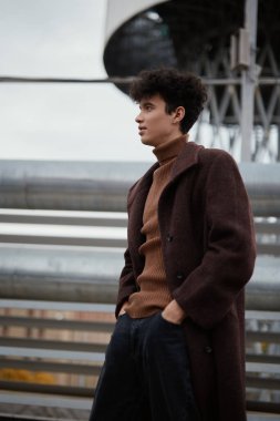 Moda genç adam kahverengi ceketli kaplumbağa yakalı kazak ayakta duran su kulesi New York.