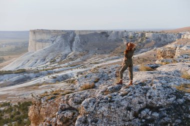 Uçurumun kenarında duran kadın, kollarını açmış, doğanın ve maceranın güzelliğini kucaklıyor.