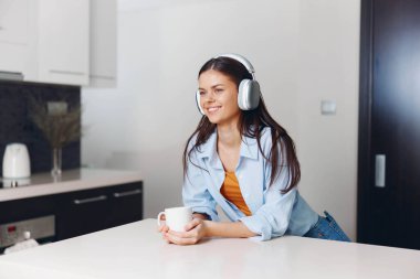 Mutfakta güzel genç bir kadın kulaklıkla müzik dinliyor.